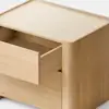 A light wooden box-shaped nightstand with a single drawer partially open, placed on a light gray surface against a plain white background.