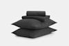A neatly folded set of dark gray bed sheets and pillowcases placed on top of two stacked matching pillows, all against a plain white background.