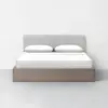 A modern bed with a light gray upholstered headboard, white bedding, and two pillows, set on a wooden platform base against a plain white wall in a minimalist room.