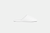 A single white slipper with a closed toe and open back is shown in a side view on a plain, light gray background.