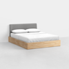 A modern bed with a light wood frame, a gray upholstered headboard, and white bedding with two pillows, set against a plain white wall and floor.