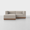 A modern, light gray sectional sofa with clean lines and a wooden base, set in a minimalistic, white room with a smooth floor.