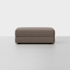 A rectangular, brown upholstered ottoman with a minimalist design sits on a light-colored floor against a plain white background.