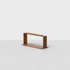 A minimalist wooden shelf with a rectangular frame and open sides, placed on a plain light gray surface against a white background.