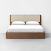 A modern wooden bed frame with a beige upholstered headboard, made up with white sheets and two white pillows, set against a plain white wall and light gray floor.