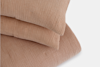 Two light brown, corduroy-textured pillows stacked on top of a matching corduroy blanket, all set against a white background.
