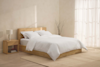 Two white pillows stacked on top of a neatly rolled white comforter, all set against a plain white background.