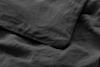 A close-up view of dark gray linen bedding, showing the texture of a pillowcase on top of a matching bedsheet. The fabric appears soft and slightly wrinkled.