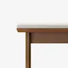 A close-up view of a wooden bench with a light-colored cushioned seat, shown against a plain white background. Only part of the bench is visible, focusing on the edge and legs.
