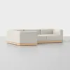 A modern, L-shaped sectional sofa with light beige upholstery and a wooden base, set against a plain, light background.