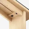 Close-up view of the underside of a light wooden table, showing the joint where the tabletop meets the leg, secured with black fasteners. The wood has a smooth, natural finish.