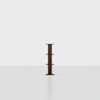 A dark brown, minimalist wooden shelving unit with four horizontal shelves stands alone in the center of a light, empty room with a white background.
