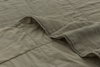 A close-up of a soft, light olive-green quilt with a slightly wrinkled texture and visible stitched squares; one corner is gently folded back.