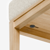 Close-up of a wooden table corner with a light-colored textured cushion on top and a black circular button or knob under the tabletop.