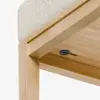 Close-up of a wooden table corner with a light-colored textured cushion on top and a black circular button or knob under the tabletop.