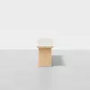 A minimalist wooden bench with a rectangular seat and solid block base, set against a plain white background and floor.