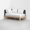 A modern daybed with a light wooden frame, dark gray backrest, and three large white pillows, positioned in a minimalistic, bright room with light gray flooring and white walls.