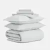 A neatly stacked light gray bedding set, including two folded pillowcases, two pillows, a folded flat sheet, a fitted sheet, and a comforter, all arranged on a white background.