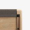 Close-up of the corner of a wooden object, possibly a table or bench, with a gray cushioned or felt pad covering the top edge. The corner features smooth, rounded wood and visible black fasteners. Background is plain white.