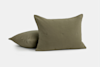 Two olive green, square throw pillows with a subtle grid texture and tufted details, one pillow standing upright and the other lying flat against a plain white background.