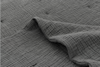 Close-up view of a gray, textured fabric with a crinkled, grid-like pattern. One section of the fabric is slightly lifted, creating gentle folds and shadows.
