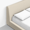 Minimalist photo of a beige upholstered bed with a tall, softly curved headboard, white pillows, and white bedding, set against a white wall and a light gray floor.