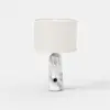 A modern table lamp with a white cylindrical fabric shade and a white marble-patterned base, featuring a small round black accent near the bottom, set against a plain white background.