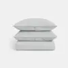 A neatly folded light gray comforter with two matching pillows stacked on top, all placed against a plain white background.