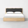 A modern wooden bed with a light wood frame, a dark gray upholstered headboard, and white bedding with two pillows, set against a plain white wall and a gray floor.