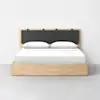 A modern wooden bed with a light wood frame, a dark gray upholstered headboard, and white bedding with two pillows, set against a plain white wall and a gray floor.
