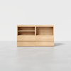 A light wooden cabinet with two open shelves on top and four closed drawers below, set against a plain white background on a gray floor.