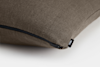 Close-up of a brown textured pillow with a visible black zipper and a small fabric tag labeled THUMA on a white background.