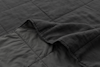 A close-up of a dark gray, quilted, textured blanket with one corner folded over, showing the stitching and soft fabric.