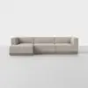 A modern, light beige L-shaped sectional sofa with clean lines and a low wooden base, set against a plain white background and floor.