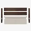 Disassembled dark wood bed frame parts and a light beige upholstered headboard laid out on a white background.