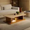 A modern living room with a light gray sofa, a wooden coffee table holding a candle, books, and a small plant, all set on a light rug with a pouf and shelves in the background.