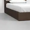 A close-up of a modern bed with a dark wooden frame, white bedding, and a white pillow, set on a light gray floor against a plain white wall.