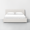 A modern, minimalist bed with a light beige upholstered headboard and base, neatly made with white bedding and two pillows, positioned against a plain white wall on a gray floor.