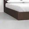 Close-up of the corner of a dark wooden bed frame with white bedding and pillows, placed on a light gray floor against a plain white wall.