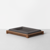 A modern pet bed with a dark gray cushioned center and a low, rectangular wooden frame, set on a light gray floor against a plain white background.