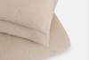 Two beige, textured pillows with a crinkled fabric surface are stacked on top of each other against a white background.