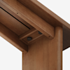 Close-up view of the underside of a wooden table showing the joint where the tabletop meets the leg, with visible screws and smooth, polished wood grain.