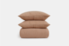 A neatly stacked set of two brown, textured pillows on top of a matching folded quilt, all displayed against a plain white background.