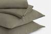 A neatly folded olive green duvet cover and two matching pillowcases are stacked on top of each other against a plain white background.
