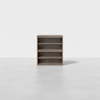 A front-facing view of a simple, modern wooden bookshelf with three shelves, standing alone on a smooth, light-colored floor against a plain white background.