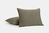 Two olive green square pillows with a subtle stitched grid pattern are displayed against a plain white background; one pillow is upright while the other leans behind it.