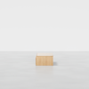 A minimalist wooden rectangular bench sits centered on a smooth, light gray floor against a plain white background.