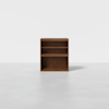 A small, rectangular wooden bookshelf with two shelves and an open bottom compartment, placed on a plain light gray floor against a white background.