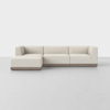 A modern, L-shaped sectional sofa with light beige upholstery and a low wooden base, set against a plain white background.