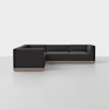 A modern, dark gray L-shaped sectional sofa with low arms and back, set on a light wooden base, positioned on a smooth, light-colored floor against a plain white background.